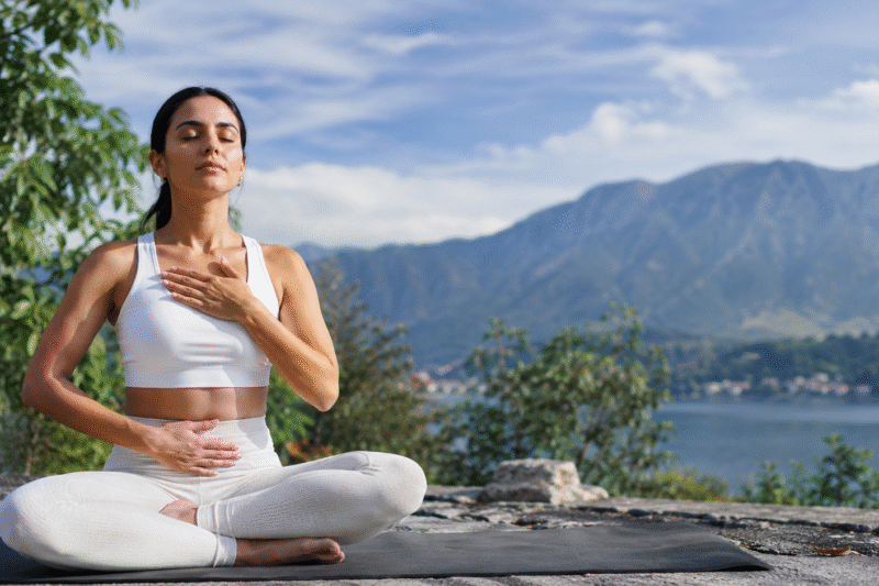 Woman practicing pranayama for anxiety outdoors with mindful deep breathing to calm the nervous system in a peaceful natural setting.Woman practicing pranayama for anxiety outdoors with mindful deep breathing to calm the nervous system in a peaceful natural setting.