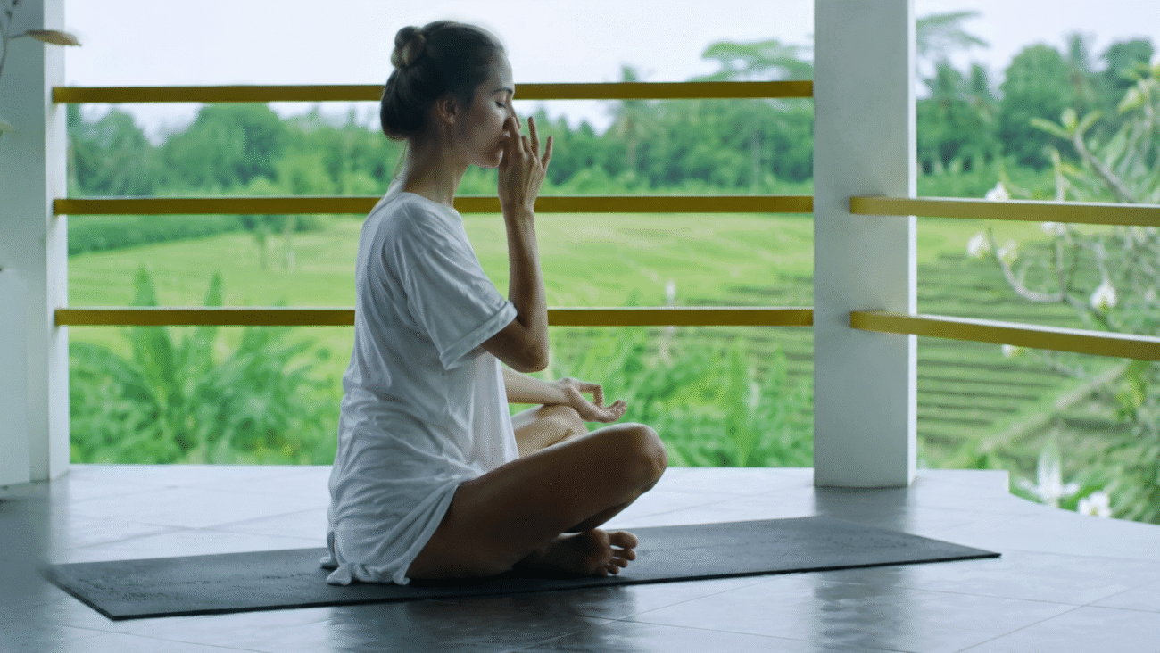 Woman practicing alternate nostril pranayama in a peaceful natural yoga retreat surrounded by lush greenery