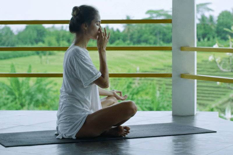 Woman practicing alternate nostril pranayama in a peaceful natural yoga retreat surrounded by lush greenery